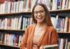 mulher sorrindo segurando um livro em uma biblioteca