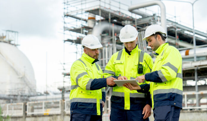 Engenheiros estão em frente à fábrica petroquímica e usam tablet para discutir seu trabalho.